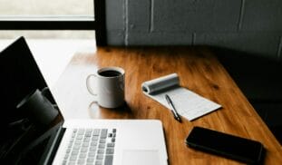 MacBook Pro, white ceramic mug,and black smartphone on table